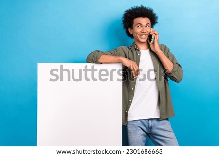 Photo of young promoter man speaking phone with friends recommend paper placard mockup free extra bonus isolated on blue color background