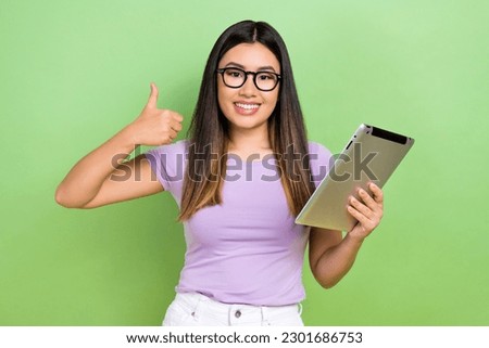 Photo of attractive japanese korean young woman hold tablet thumb up specs wear trendy purple clothes isolated on green color background
