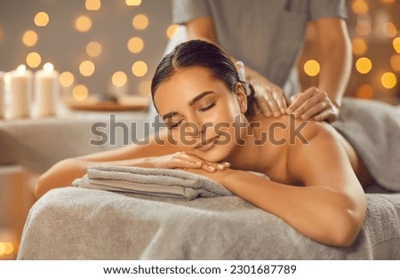 Woman enjoying professional body massage at a modern spa salon. Relaxed young lady lying on a massage table while a skillful masseuse is gently massaging her back. Beauty, health, pleasure, concept Royalty-Free Stock Photo #2301687789