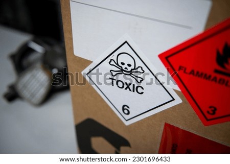 White label with toxic warning symbol on a box with a mask in the background.