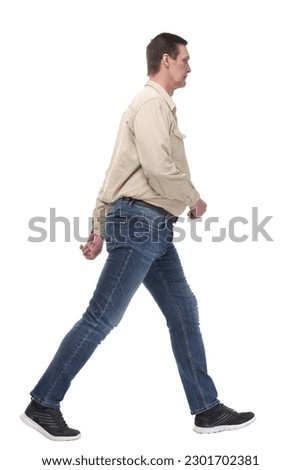 full length side view picture of a casual young man walking looking at camera