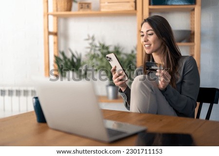 Smiling young woman looking at smart phone screen holding credit card, using mobile phone secured online e-banking app, satisfied with online cashback purchase or good electronic banking services. Royalty-Free Stock Photo #2301711153