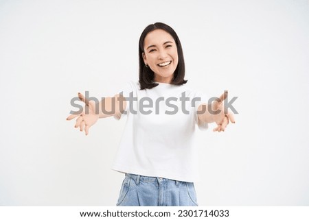 Friendly smiling asian woman, reaching her hands towards camera, hugging, welcoming you, standing over white background.