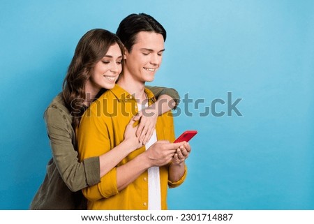 Photo of smiling satisfied two people wife with husband embracing trust reading browsing news smartphone internet isolated on blue color background
