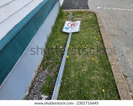 A handicap zone sign and post lying on the grass after being broken off.