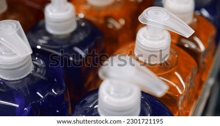 Rows unbranded transparent colorful bottles of consumer cosmetics with pumps. Unlabelled dark blue and orange shampoo or liquid soap in consumer packaging without logo. High quality photo Royalty-Free Stock Photo #2301721195