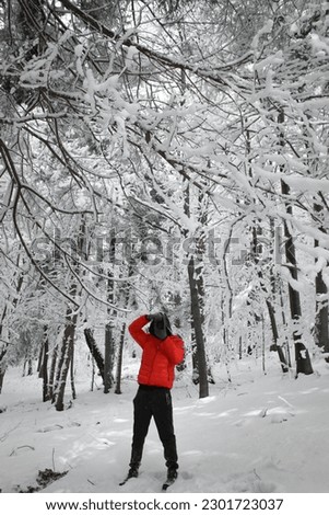 Mystery person in orange jacket with camera in the snowy forest