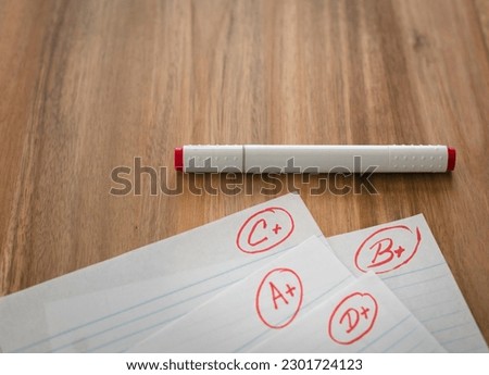 Different grades school paper marked in red ink over a wood desktop.