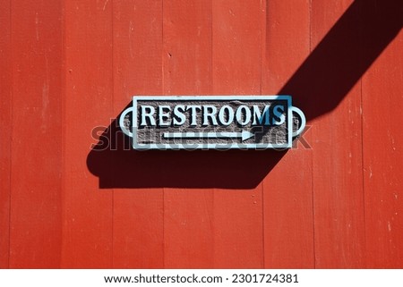 sign restroom in metal at a red wall with shadow