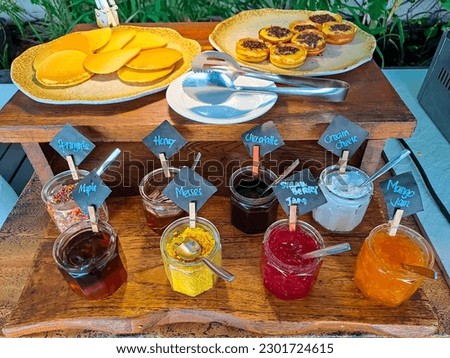 Pancake and sweet martabak with many kind of jams arranged on a wooden ladder table, fresh and green plants in the background. Set of breakfast menu in the hotel or all you can eat restaurant