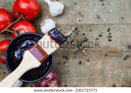 BBQ sauce in a wood bowl with brush over top an old rustic wood table  background with free space for text Image shot from overhead view.