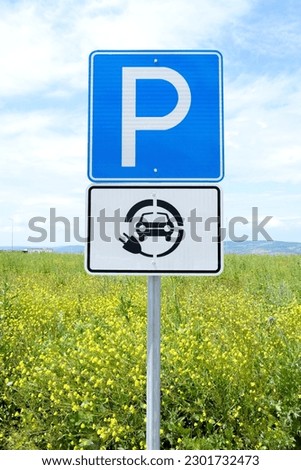 Parking and electric car charging points sign with green area and sky background. 