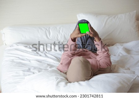 Portrait of a beautiful young Asian Muslim woman wearing hijab on bed holding mobile phone