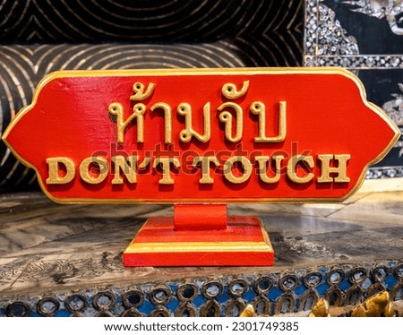 A red sign with the words DON'T TOUCH in both Thai and English is seen up close at the Wat Pho temple in Bangkok, Thailand. Translation Thai to English: Don't Touch. Royalty-Free Stock Photo #2301749385