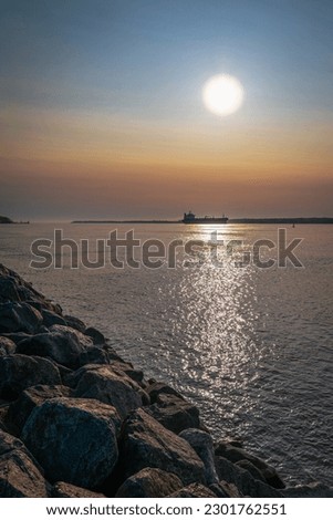 Trois-Rivières sunrise landscape over the rocky riverbank at St Lawrence River, industrial carrier ship cruising along the horizon in Quebec, Canada