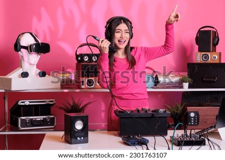 Cheerful performer talking into microphone with fans while mixing electronic sounds with techno, enjoying club party at night. Asian artist creating musical performance with remix music