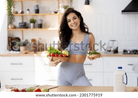 Beautiful smiling woman holding bowl with fresh vegetable standing in modern kitchen, looking at camera. Vegetarian diet, healthy lifestyle concept Royalty-Free Stock Photo #2301775919