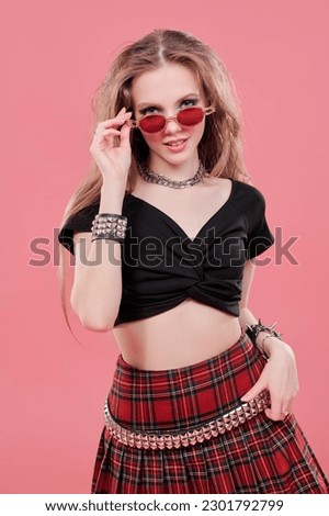 Youth fashion and lifestyle. Youth pop and rock culture. Glamorous teenage girl with bright makeup and rock-style hair styling poses against a pink studio background.