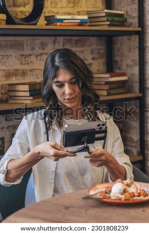 A young positive woman food blogger eating in a cafe,live broadcast using a smartphone and a neck phone holder.