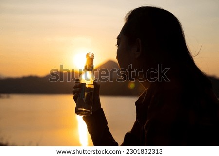 Silhouette woman holding a beer bottle on the beach at sunset Royalty-Free Stock Photo #2301832313