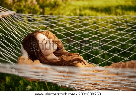 a woman is resting lying in a mesh hammock with her hands behind her head, smiling happily, enjoying a warm day in the rays of the setting sun, lying in an orange dress