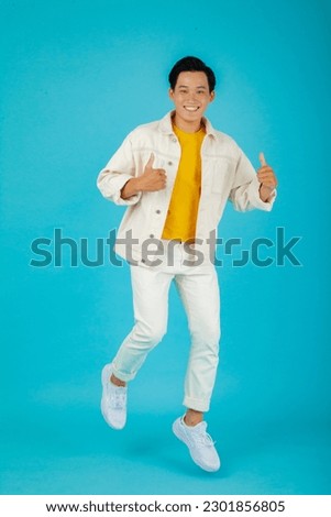 Full length portrait of smiling young handsome Asian man pointing fingers to empty space aside in isolated studio light blue background