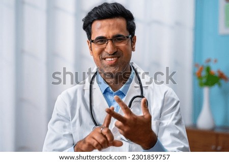 Confident indian doctor talking on video call by looking at camera from hospital with patients - concept of online counseling, medical advice and consultation Royalty-Free Stock Photo #2301859757