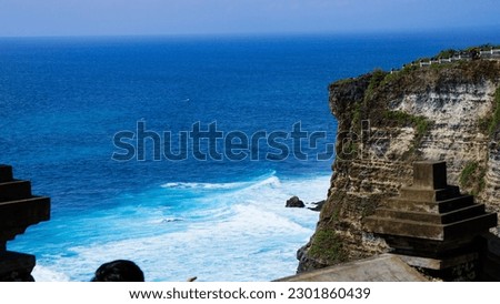Blue sea waves rushing to produce sea foam and limited by high cliffs on a sunny afternoon, producing a stunning dramatic effect, located in Uluwatu, Bali, Indonesia