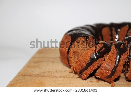 A picture of a chocolate cake, with a chocolate topping melting all the way down, on a wooden plate with a white background