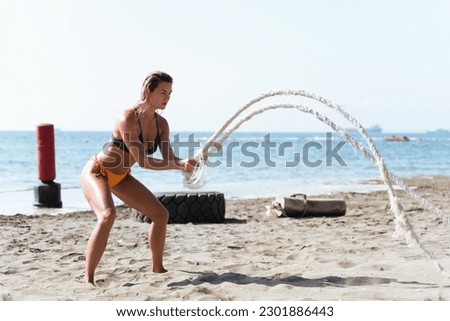 Young woman athlete exercising with battling rope during her workout at a beach gym.
