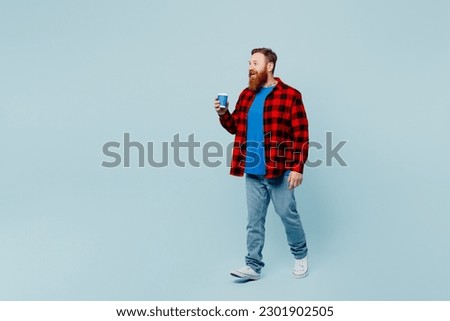 Full body young redhead bearded man wear casual clothes hold takeaway delivery craft paper brown cup coffee to go isolated on plain pastel light blue cyan background studio portrait. Lifestyle concept