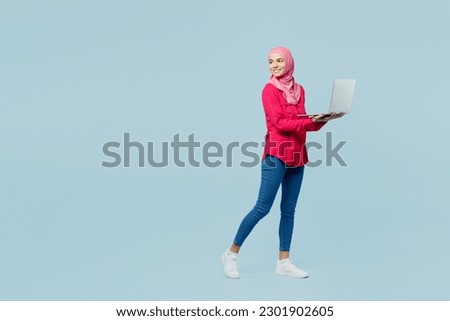 Full body young arabian asian muslim IT woman wear pink abaya hijab work use hold laptop pc computer look aside isolated on plain pastel blue cyan background studio. People uae islam religious concept Royalty-Free Stock Photo #2301902605