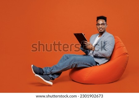 Full body young employee business man corporate lawyer in formal grey suit shirt work in office sit in bag chair clipboard with paper account documents isolated on plain red orange background studio Royalty-Free Stock Photo #2301902673