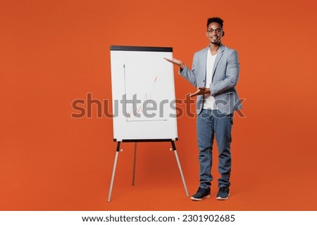 Full body young employee business man corporate lawyer wear classic formal grey suit shirt glasses work in office use point on flipchart graph on marker board isolated on plain red orange background Royalty-Free Stock Photo #2301902685