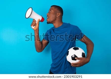 Funny Young man wearing blue T-shirt holding a ball over blue background People sincere emotions lifestyle concept. Mock up copy space. Screaming in megaphone.