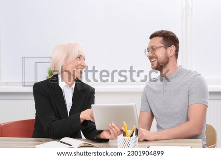 Happy boss with tablet and employee discussing work issues at wooden table in office