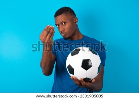 Young man wearing blue T-shirt holding a ball over blue background Doing Italian gesture with hand and fingers confident expression