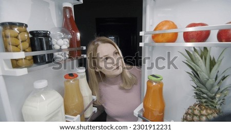 Middle-aged woman peeking inside the refrigerator late at night Royalty-Free Stock Photo #2301912231