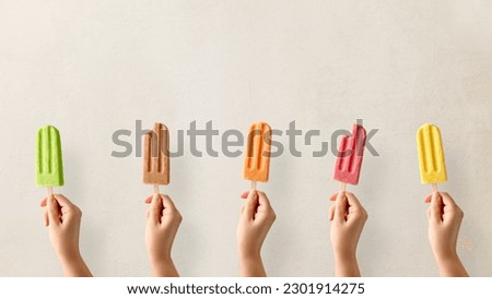 Hands holding different types of colorful fruit popsicles. Strawberry, mango, caramel, apple and orange flavor