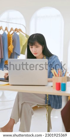 asian female fashion designer use drawing tablet and computer to design dressing manuscripts - there are a lot of beautiful clothes in her studio