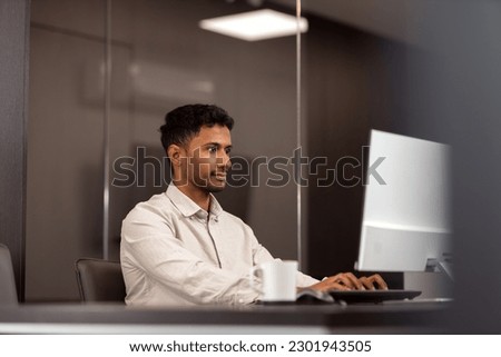 A multiethnic lawyer is working on a desktop computer in an elegant office.