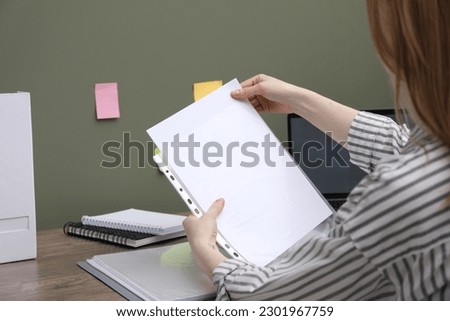 Woman putting paper sheet into punched pocket at wooden table, closeup