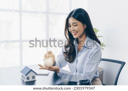 Businesswoman holding a house model .House on Hand with piggy bank.Real estate,Property insurance and security concept.Savings and finance concept. Royalty-Free Stock Photo #2301979347