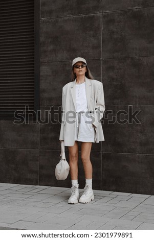 beautiful blonde girl dressed in milky oversized jacket, short gray shorts, t-shirt, beige cap, massive boots, bag in hand, accessories, sunglasses, stylish fashion outfit, full length lifestyle model Royalty-Free Stock Photo #2301979891