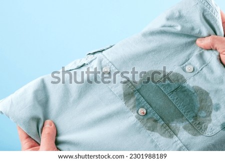Men hands showing a dirty shirt and visual evaluation of stain on clothes on a blue background. Spoiled linen. isolated. High quality photo Royalty-Free Stock Photo #2301988189
