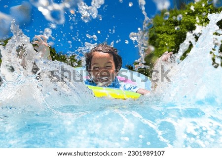 Child in swimming pool floating on toy ring. Kids swim. Colorful rainbow float for young kids. Little boy having fun on family summer vacation in tropical resort. Beach and water toys. Sun protection.