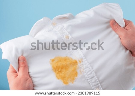 Dirty yellow stain on a white shirt. men's hands showing and visual evaluation of stain. Spoiled linen. isolated. top view. High quality photo Royalty-Free Stock Photo #2301989115
