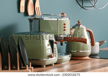 Electric kettle, coffee machine and toaster on wooden kitchen counter near green wall Royalty-Free Stock Photo #2302018275