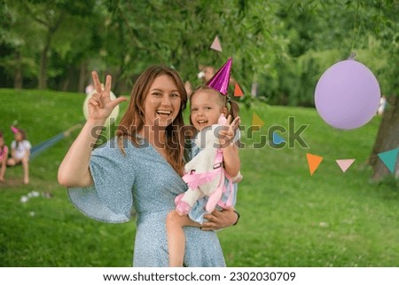 Mom and daughter in their arms show the number three with their fingers folded. A little girl with her family celebrates her birthday in nature in the park