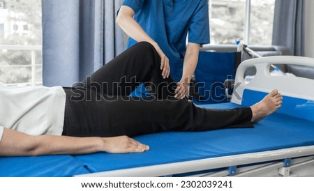 Asian female physiotherapist helping senior older woman stretching hamstring, Rehabilitation physiotherapy, elderly. Causes knee pain, swelling, redness, stiffness in knee, clunking noise in knee. Royalty-Free Stock Photo #2302039241
